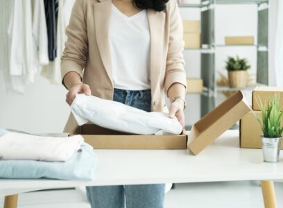 Young Asian businesswoman startup entrepreneur SME owner picking up a yellow shirt before packing it in an inner box with a customer. Online Business Ideas and Freelance.